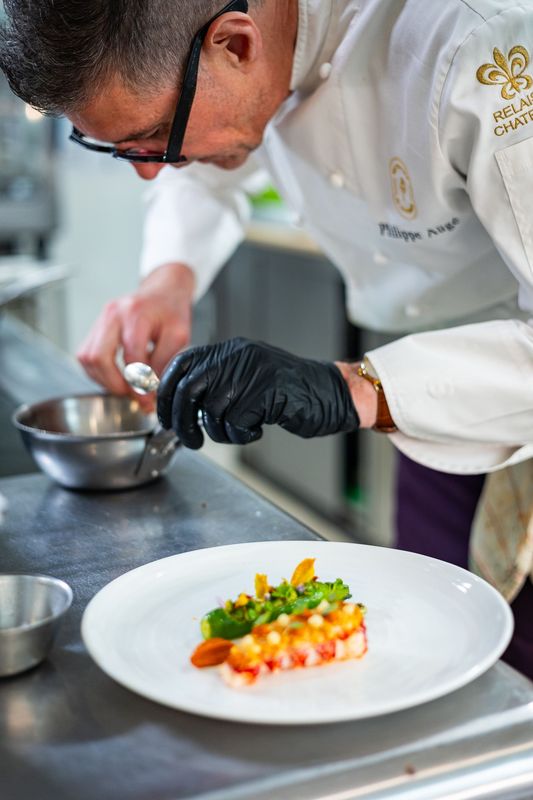 Philippe Augé, chef de l'Hostellerie de Levernois en train de dresser une assiette de Homard bleu crispy, courgette blanche et pistou gênois (©Christophe Fouquin/Hostellerie de Levernois)